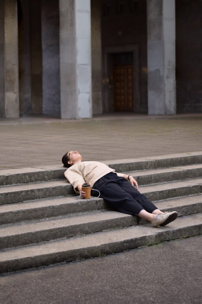 Photo by JOYUMA man in brown hoodie and black pants sitting on gray concrete stairs