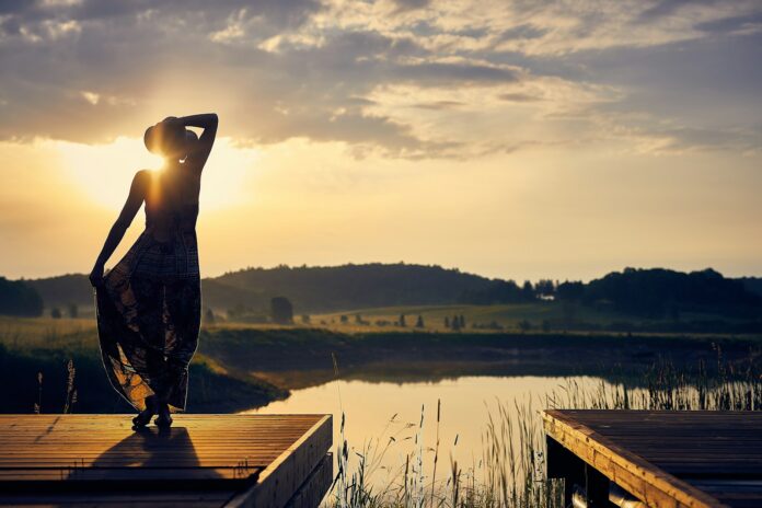 Photo by Darius Bashar silhouette of woman standing on brown wooden dock during golden hour